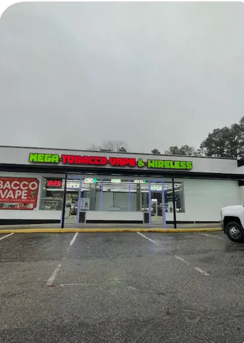 Mega Tobacco Vape & Wireless storefront in Scotland Neck NC, green and red lit sign above the entrance with open parking out front